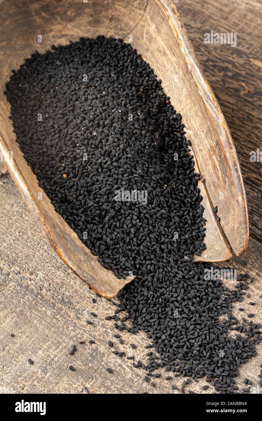 Black cumin seeds spilled from a vintage wooden scoop Stock Photo