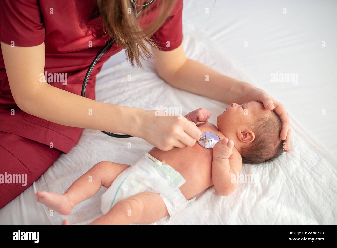 Pediatric doctor exams newborn baby girl with stethoscope in hospital Stock Photo