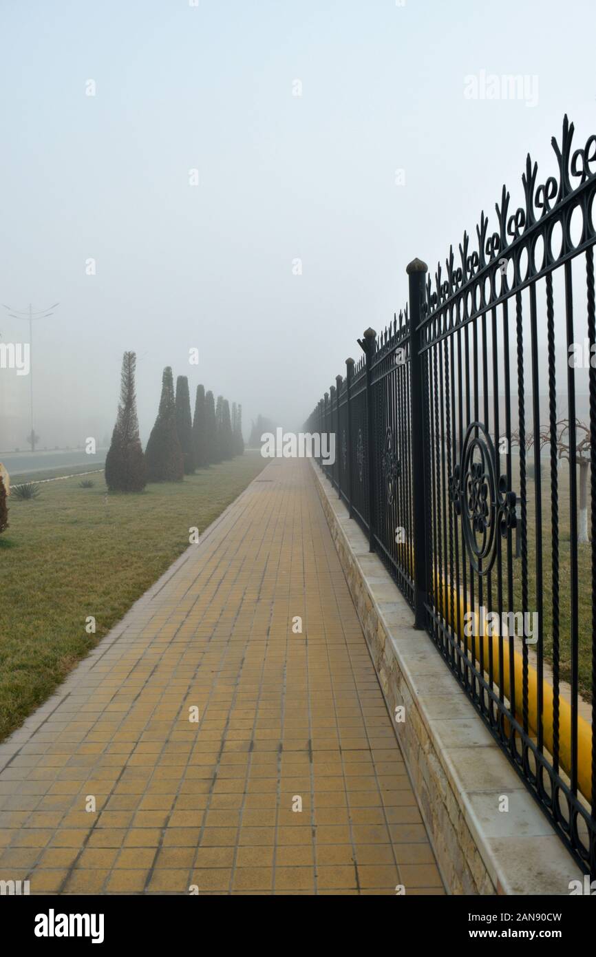 City alley with trellised fence in the morning fog Stock Photo