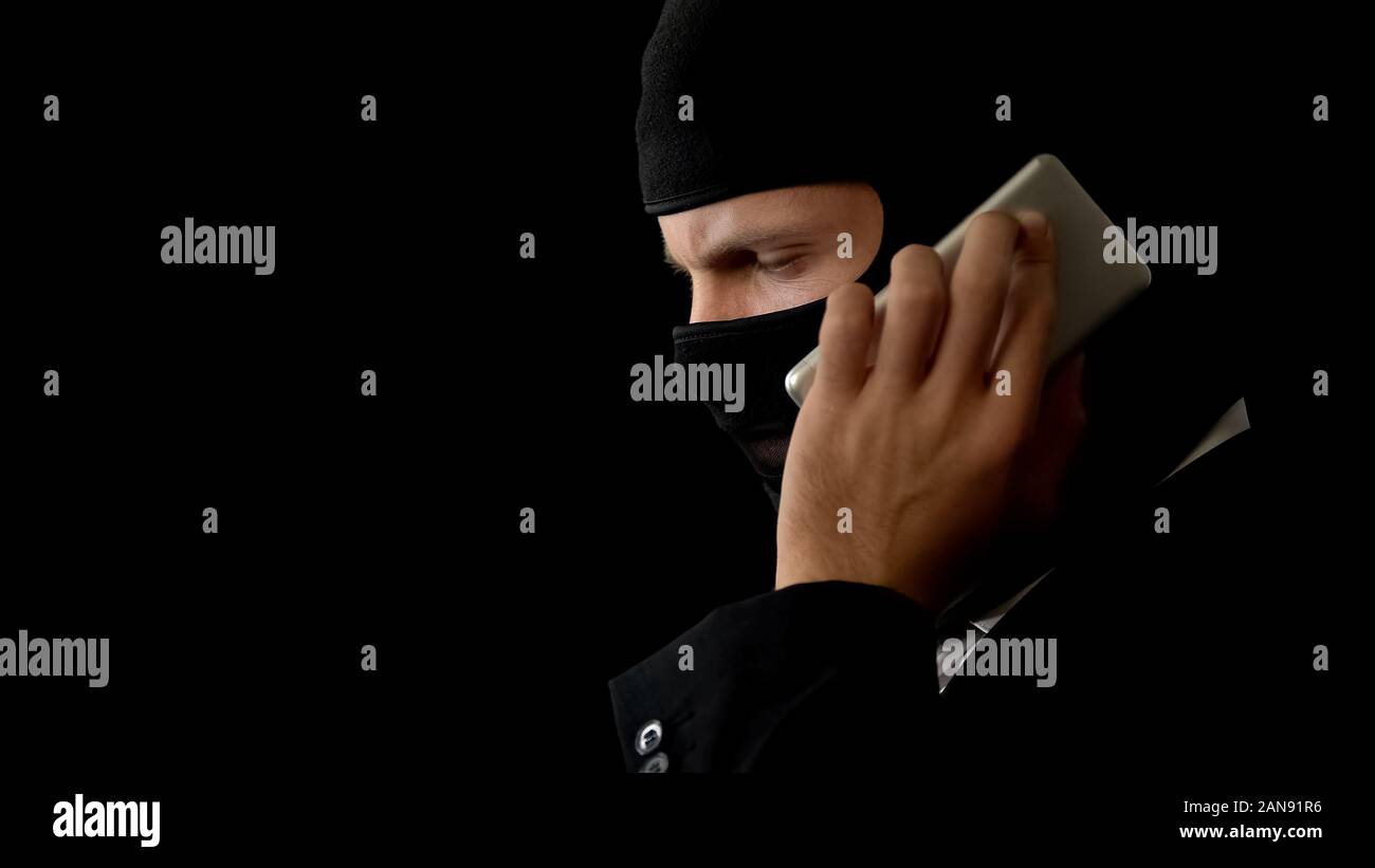 Killer in balaclava talking on phone, planning crime with partners