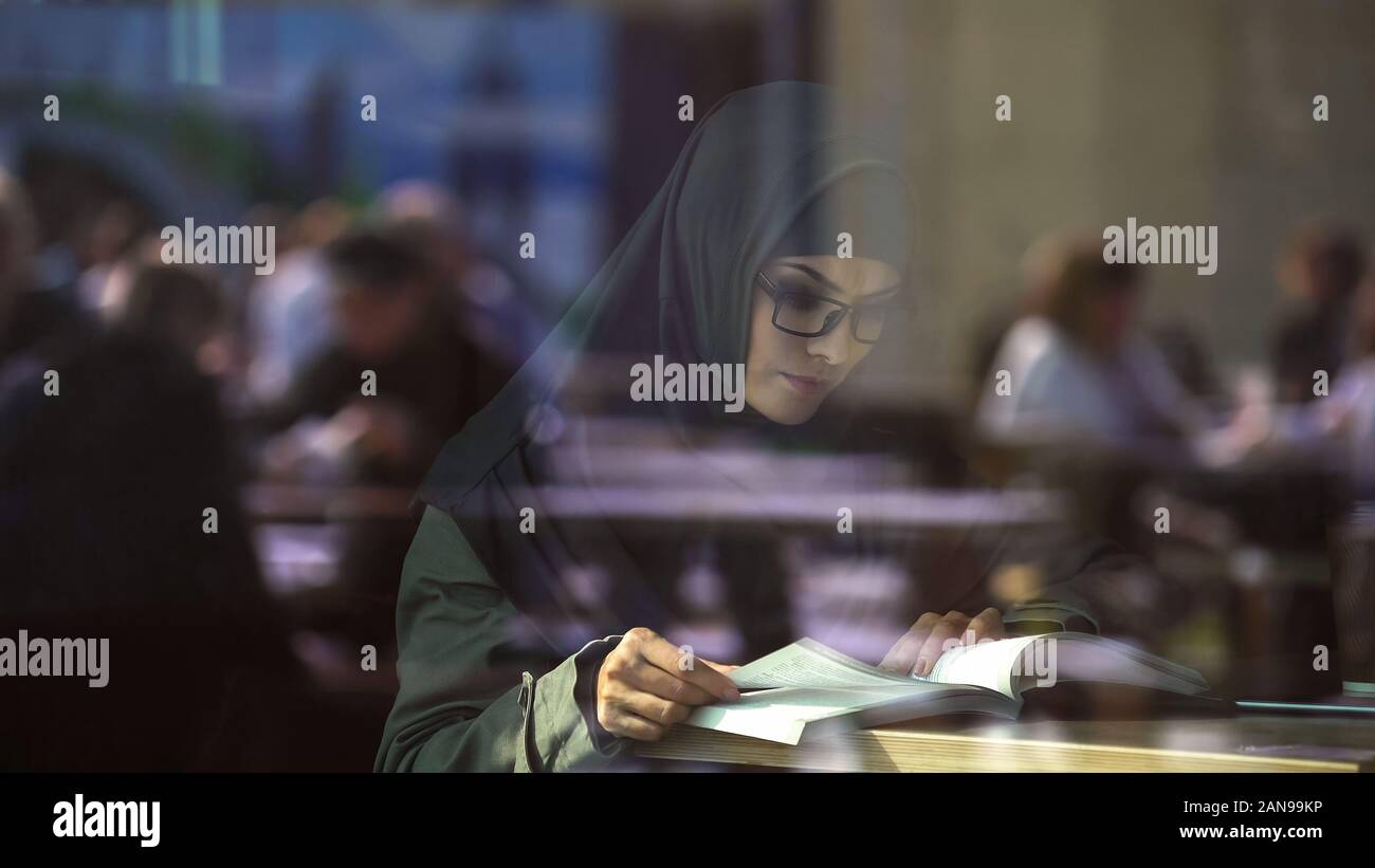 Young Arabic lady reading book in cafe, student preparing for exams, literature Stock Photo