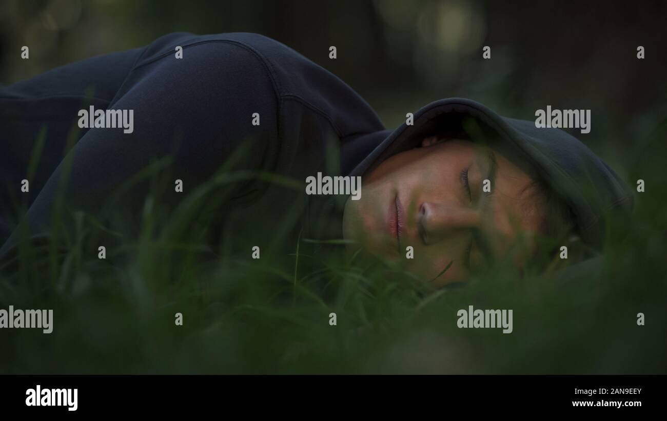 Homeless male sleeping on grass in park, poverty and social issues concept Stock Photo