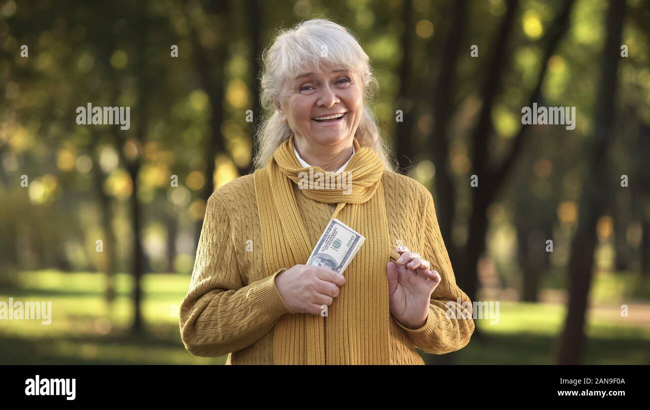 Energetic old lady holding stack of dollar bills in park, planned retirement Stock Photo