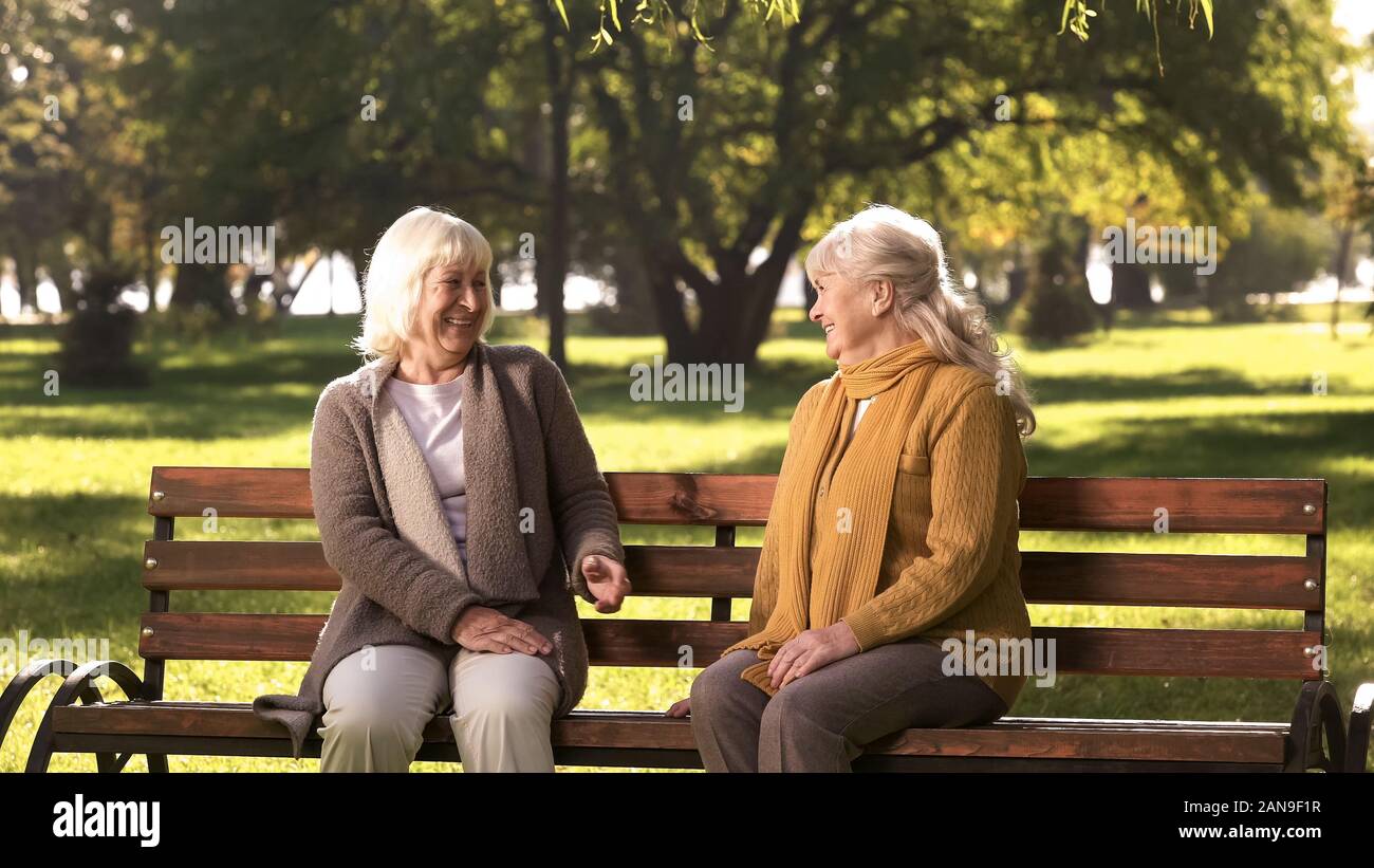 Two old fiends talking and laughing sitting on bench in park, retirement age Stock Photo