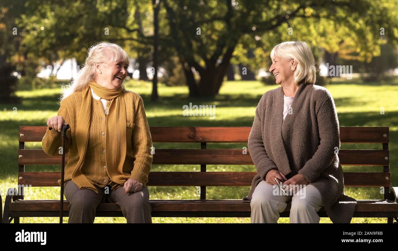 Two elderly ladies laughing and talking, sitting on bench in park, old friends Stock Photo