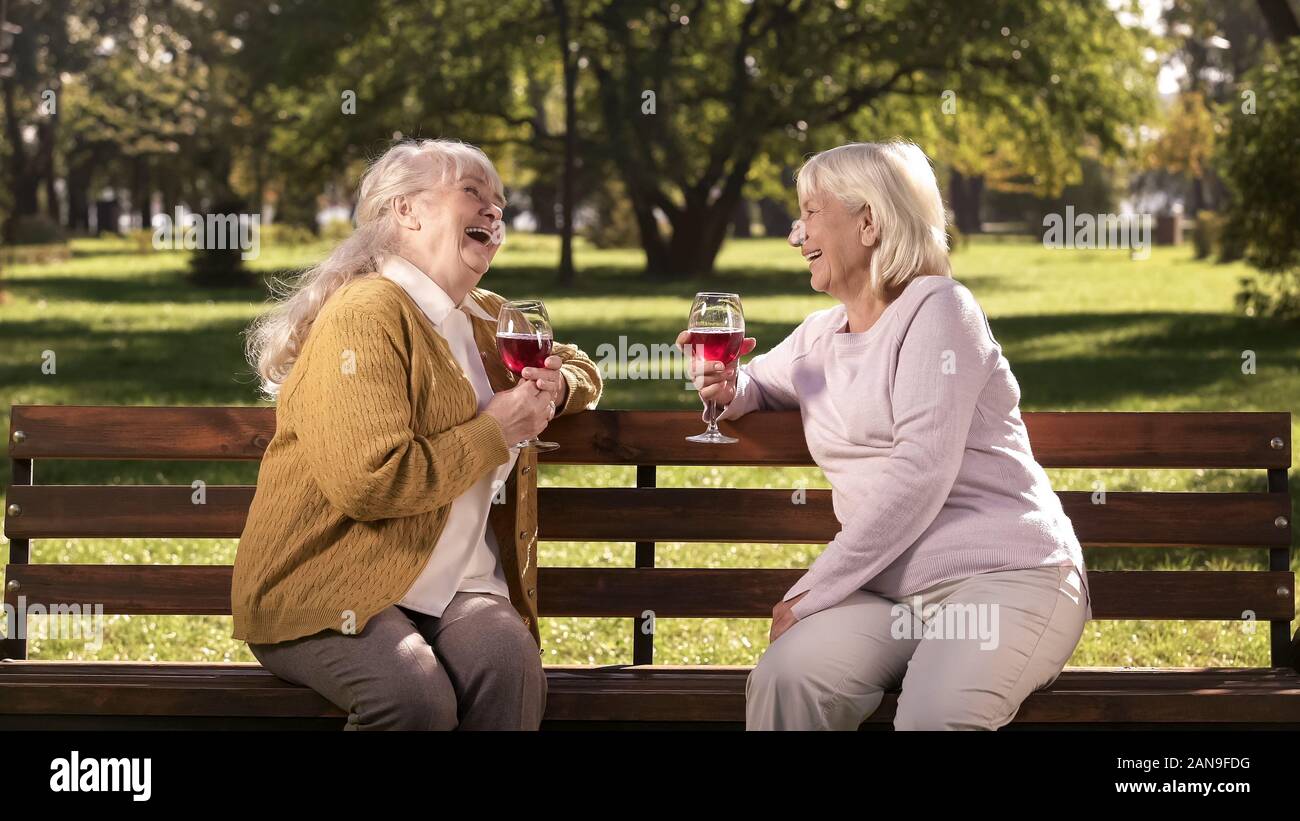 Two old ladies drinking wine and talking on bench in park, happy golden years Stock Photo