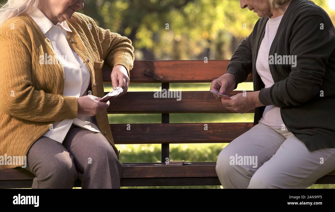 Two old women enjoying cards playing on bench in park, elderly friends leisure Stock Photo