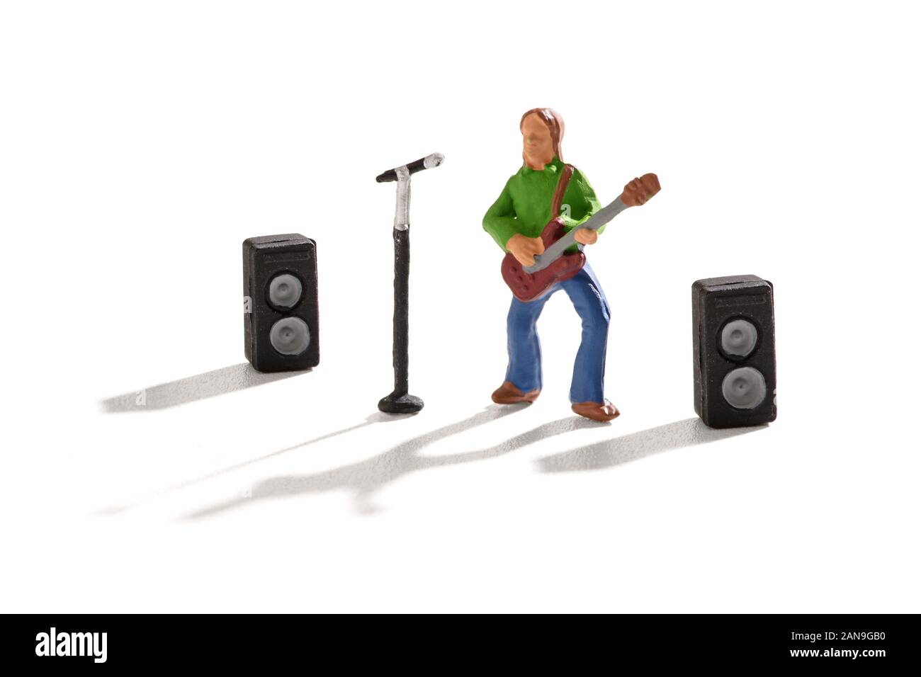 Miniature figure of a rock star playing a guitar and singing in front of a microphone and speakers in an entertainment and rock n roll music concept Stock Photo