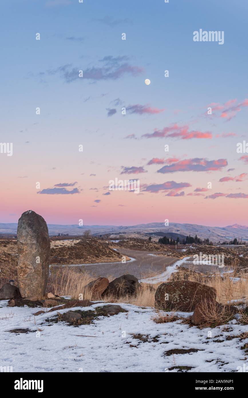 Colorful sunset over a snow covered vineyard in eastern washington with rocks and grasses in the foreground and mountains in the distance Stock Photo