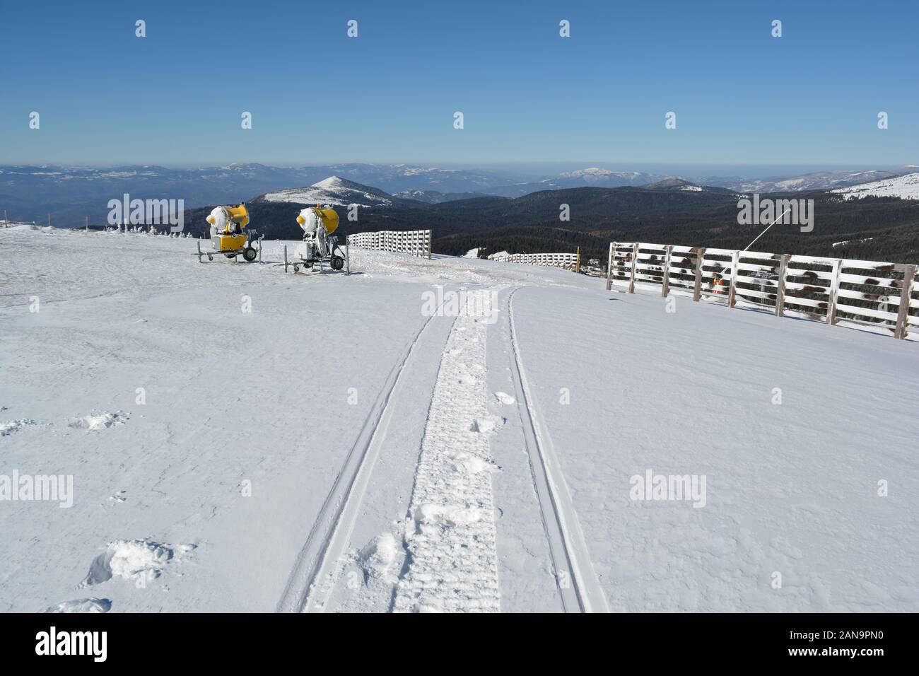 Snowmobile trail in fresh snow, snow cannons wooden fence in background and a few mountain peaks in the distance, Mt.Kopaonik, Serbia Stock Photo