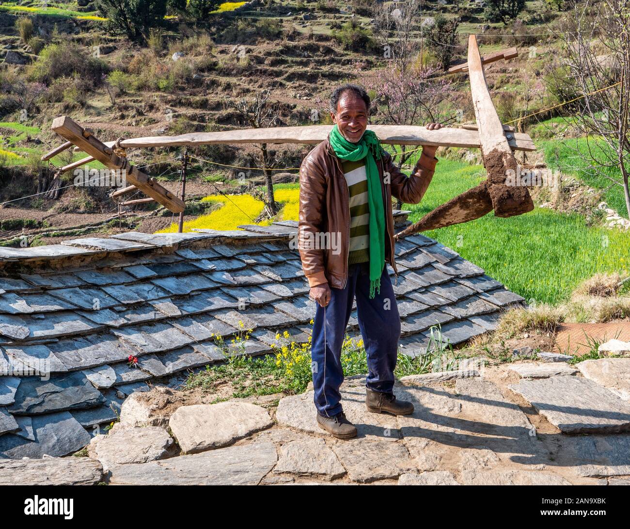 A villager of Dhurr in the Pindar Valley of Northern India casually carrying a heavy plough up a steep slope through the village Stock Photo