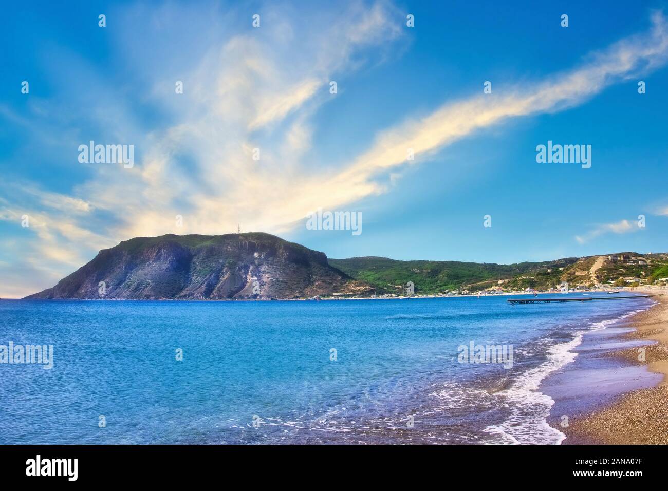 Horizontal photo with view on rock in Agios Stefanos Bay beach on famous Greek Kos island. Sky is blue with few clouds. Beach sandy with small stones. Stock Photo