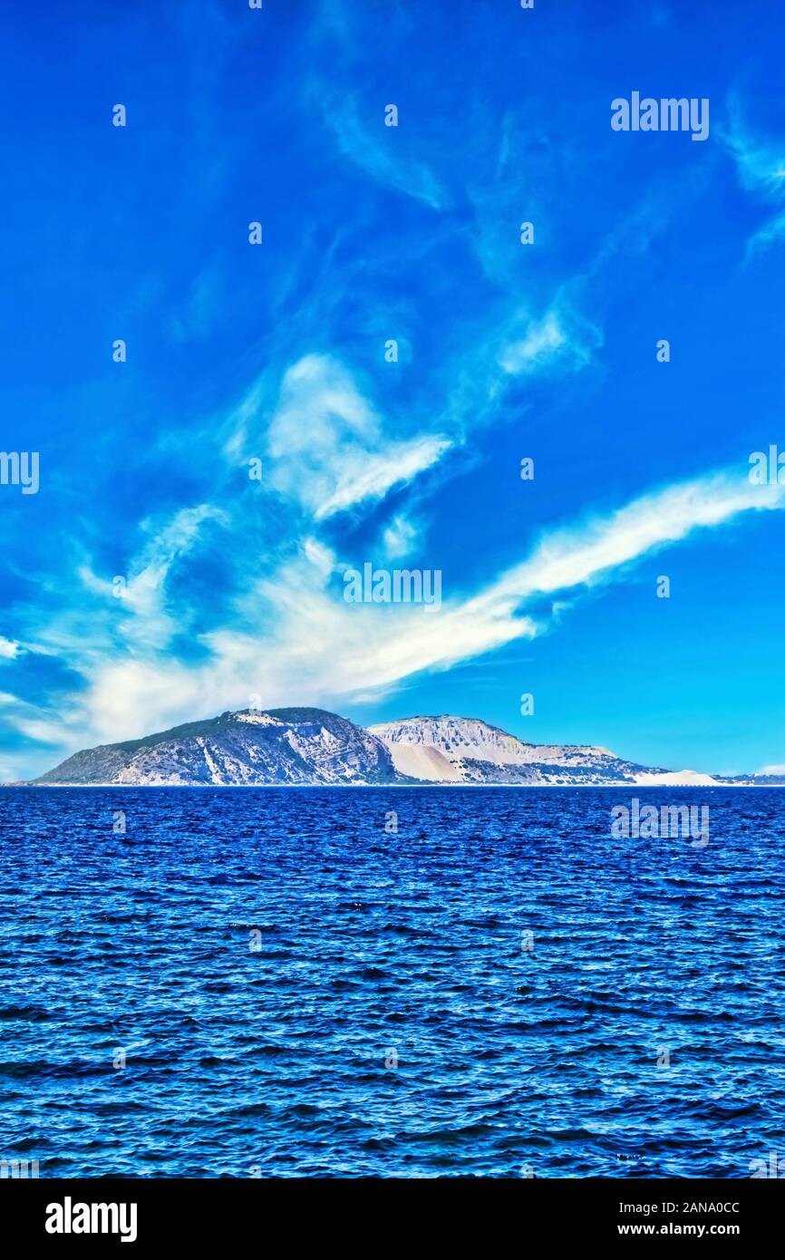 Vertical photo with view on small island in Aegean sea. Island is between Kos and Nisyros. Sky is blue with white clouds. Stock Photo
