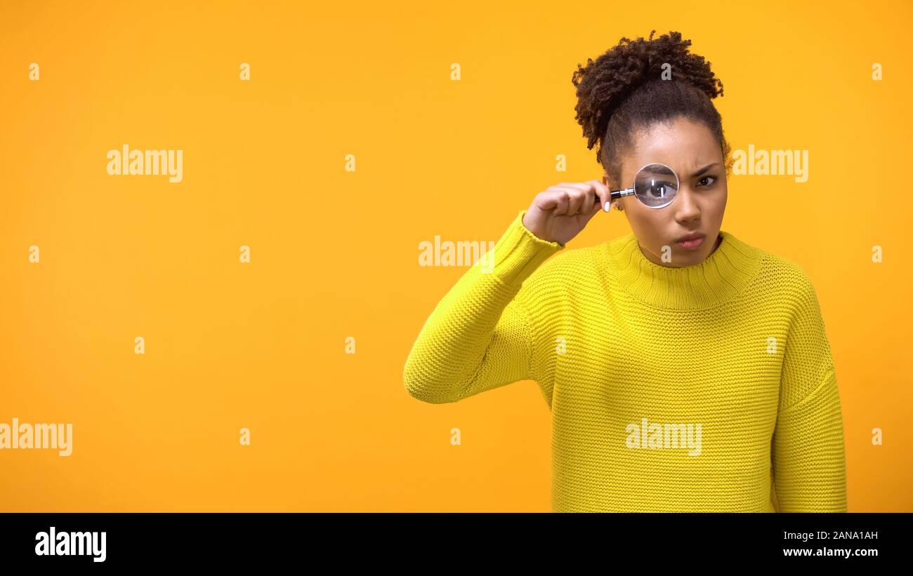 Suspecting afro-american woman looking thorough magnifying glass, inspection Stock Photo