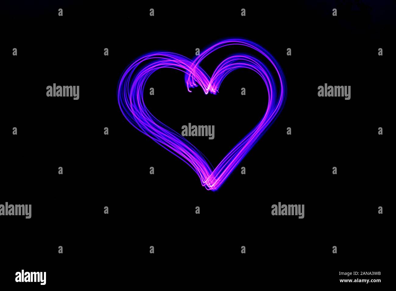 Long exposure light painting, vibrant color in a heart shape symbol abstract swirl against a clean black background.  Light painting photography. Stock Photo