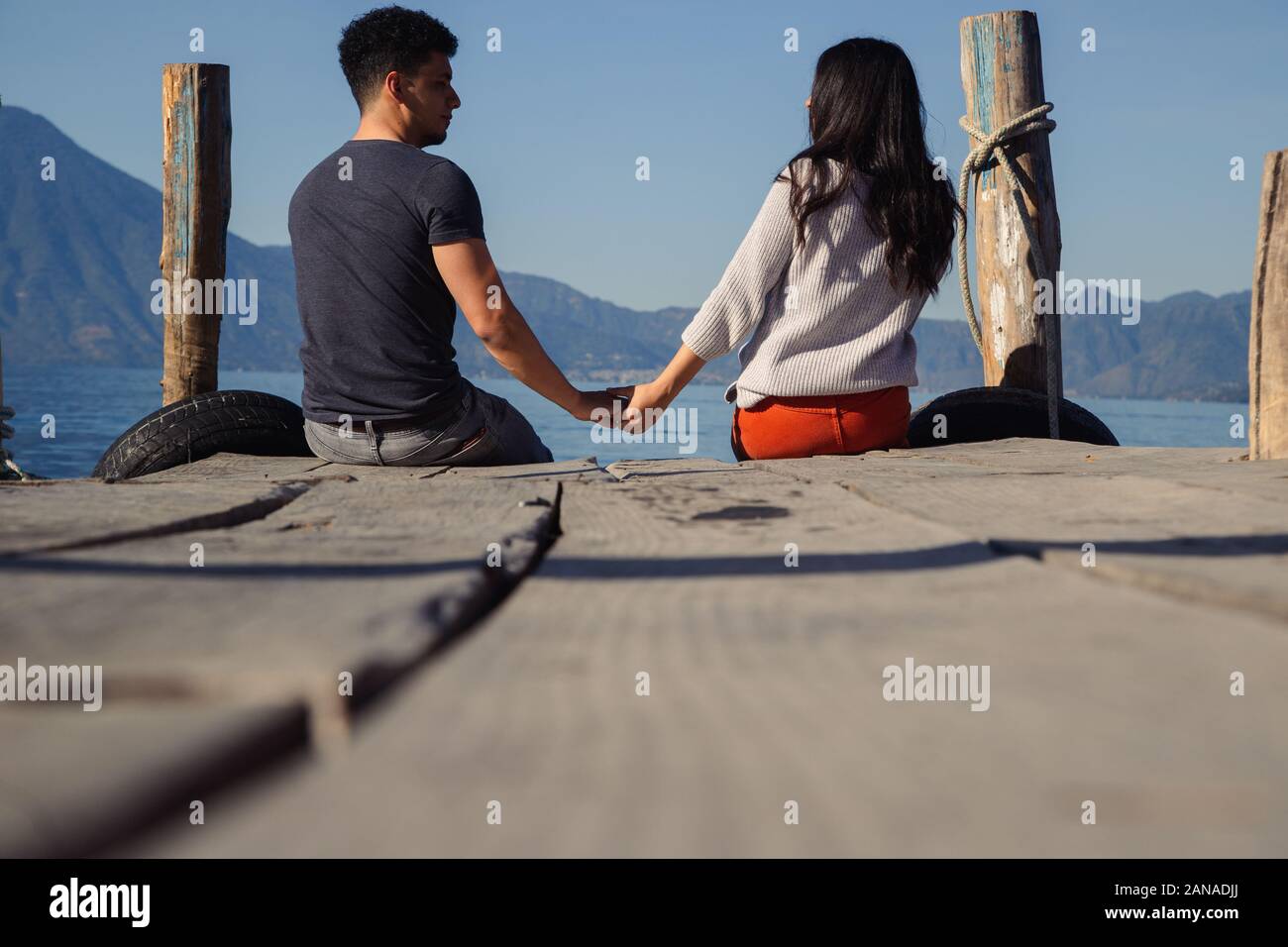 Couple sitting on the pier of Lake Atitlan in Guatemala seeing each other Stock Photo