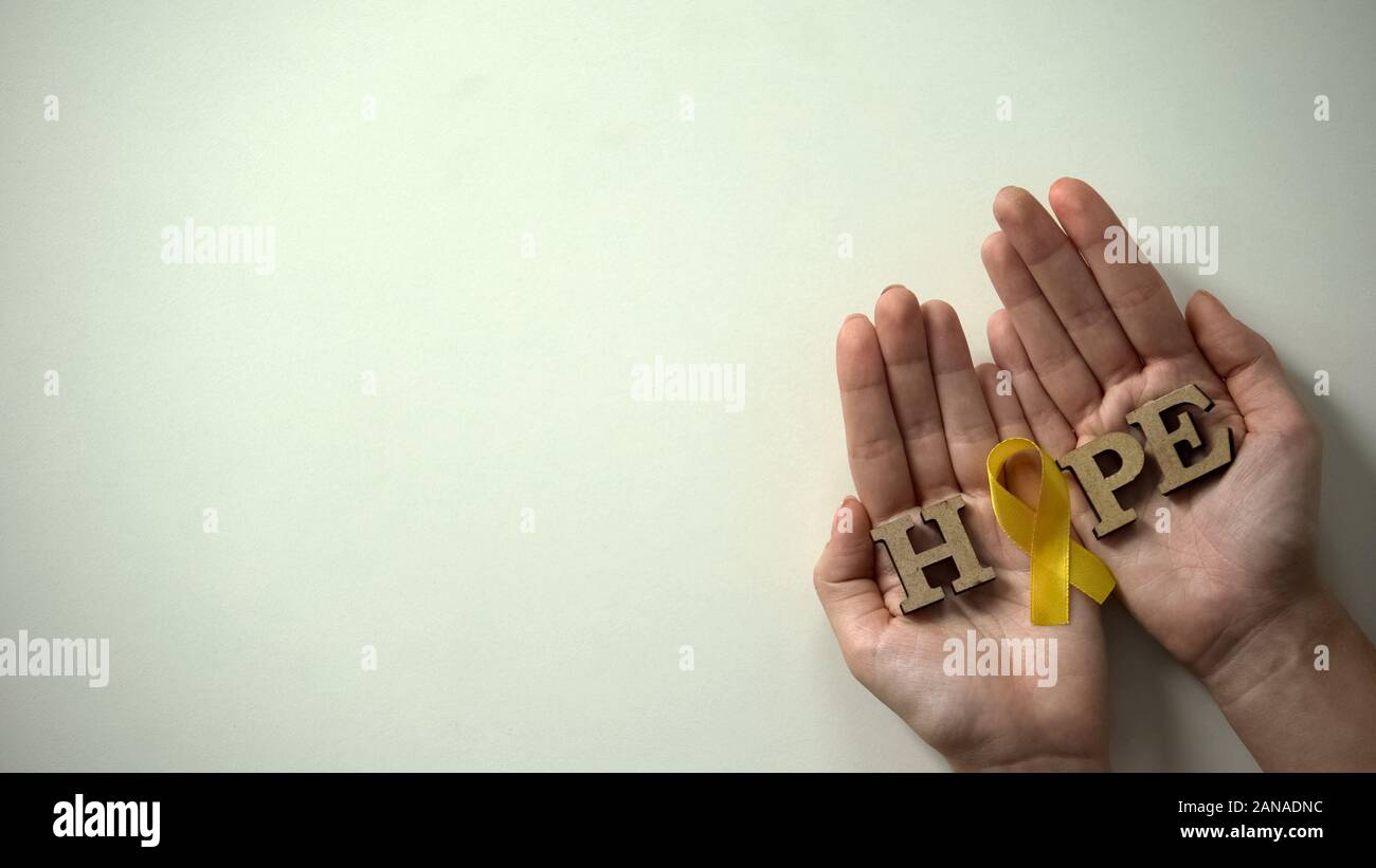 Yellow ribbon and hope word in hands, childhood cancer awareness, healthcare Stock Photo