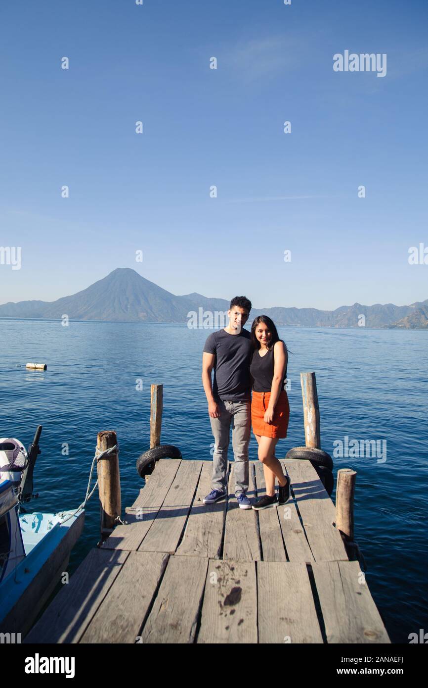 Traveling couple standing at the pier of Lake Atitlan smiling at the camera. Stock Photo