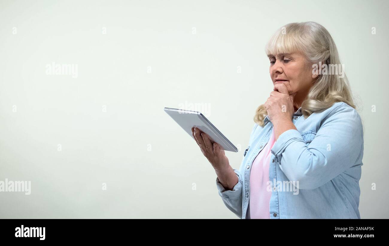Thoughtful elderly lady using tablet, online banking app, modern technologies Stock Photo