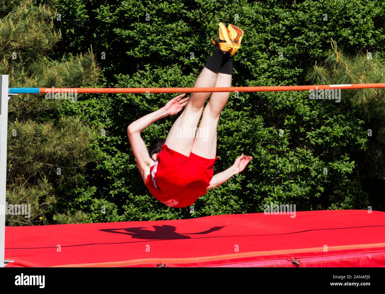 A high school track and field athlete clears the high jump bar and is about to land on the red mats. Stock Photo