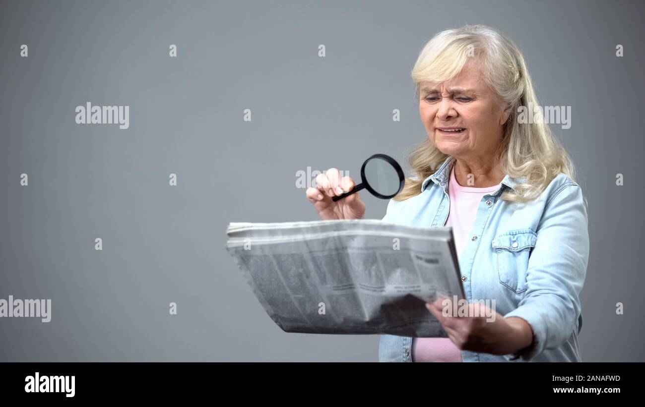 Elderly lady trying to read newspaper with magnifying glass, poor