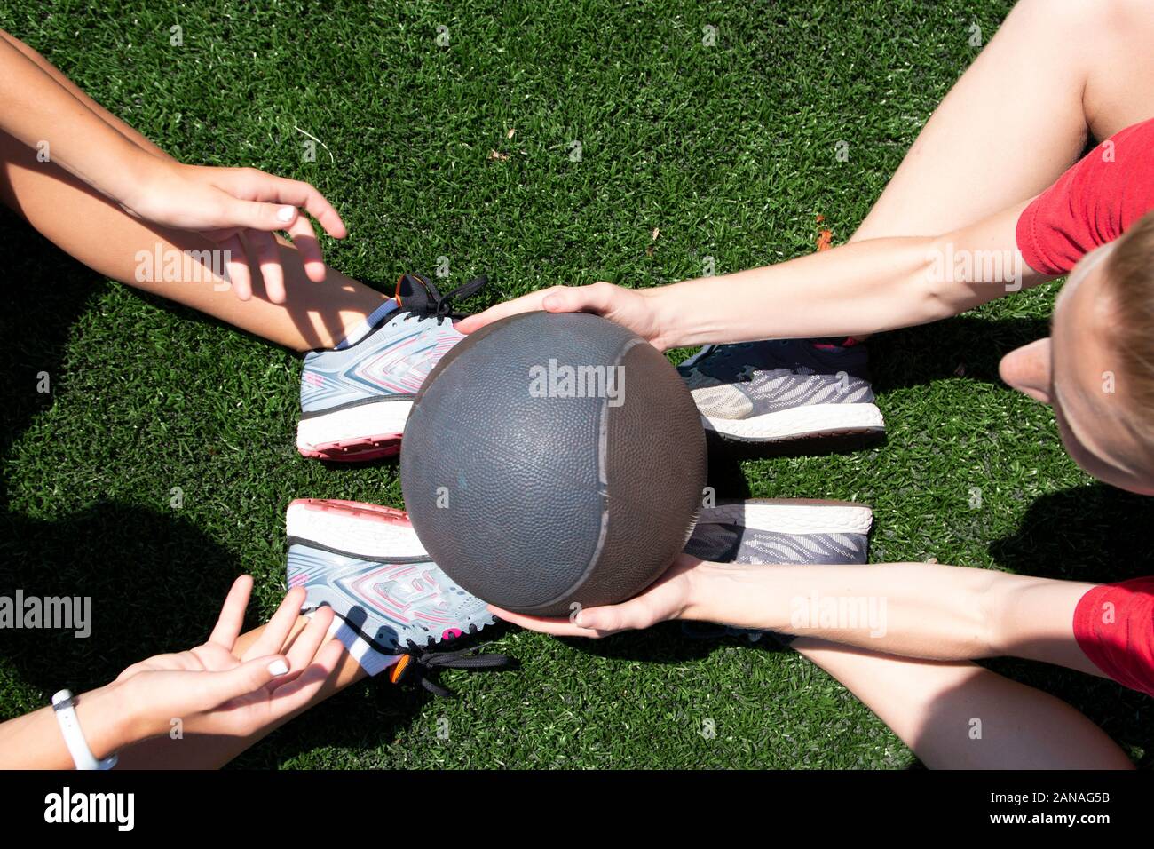 Two high school girls are passing a medicine ball while doing situps on a green turf field. Stock Photo