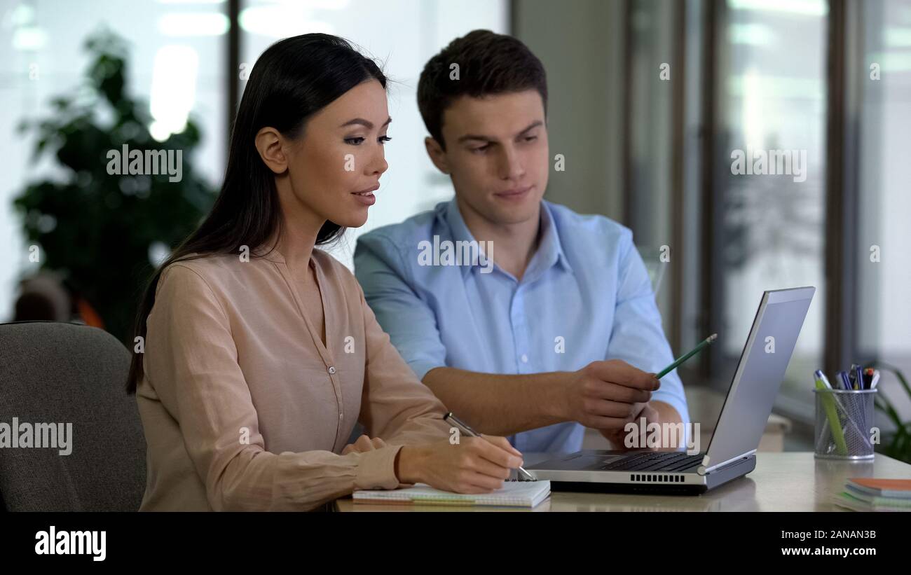Young man teaching female trainee use laptop program, office job, cooperation Stock Photo