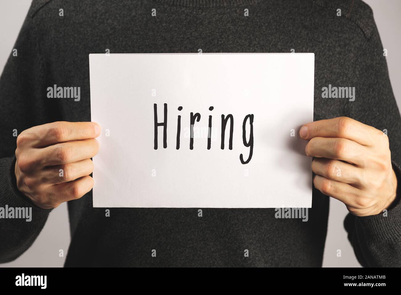 'Hiring' sign on a paper in male hands. Concept of job offer, hiring for a position at work Stock Photo