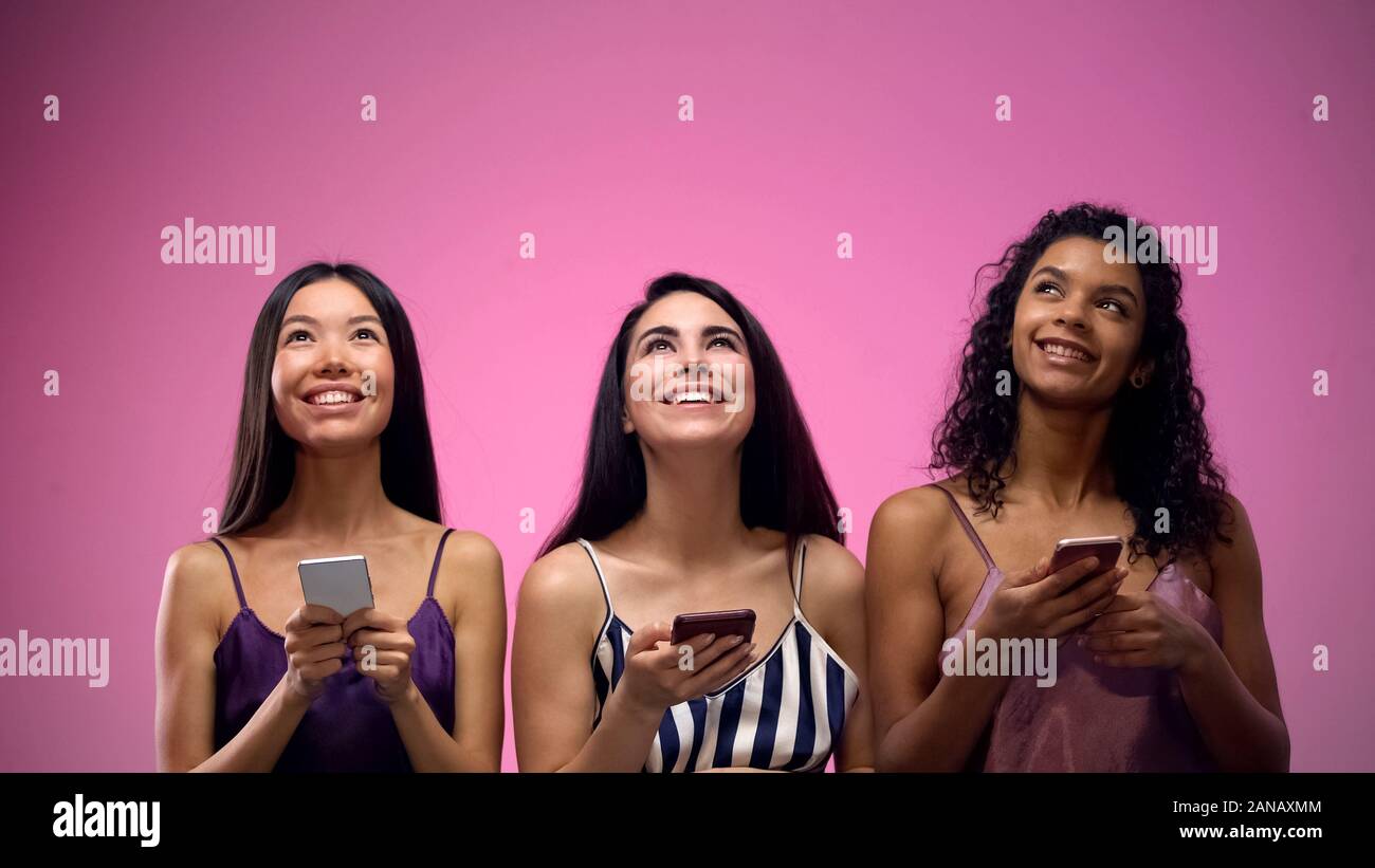 Three adorable multiracial women using mobile apps and looking up, template Stock Photo