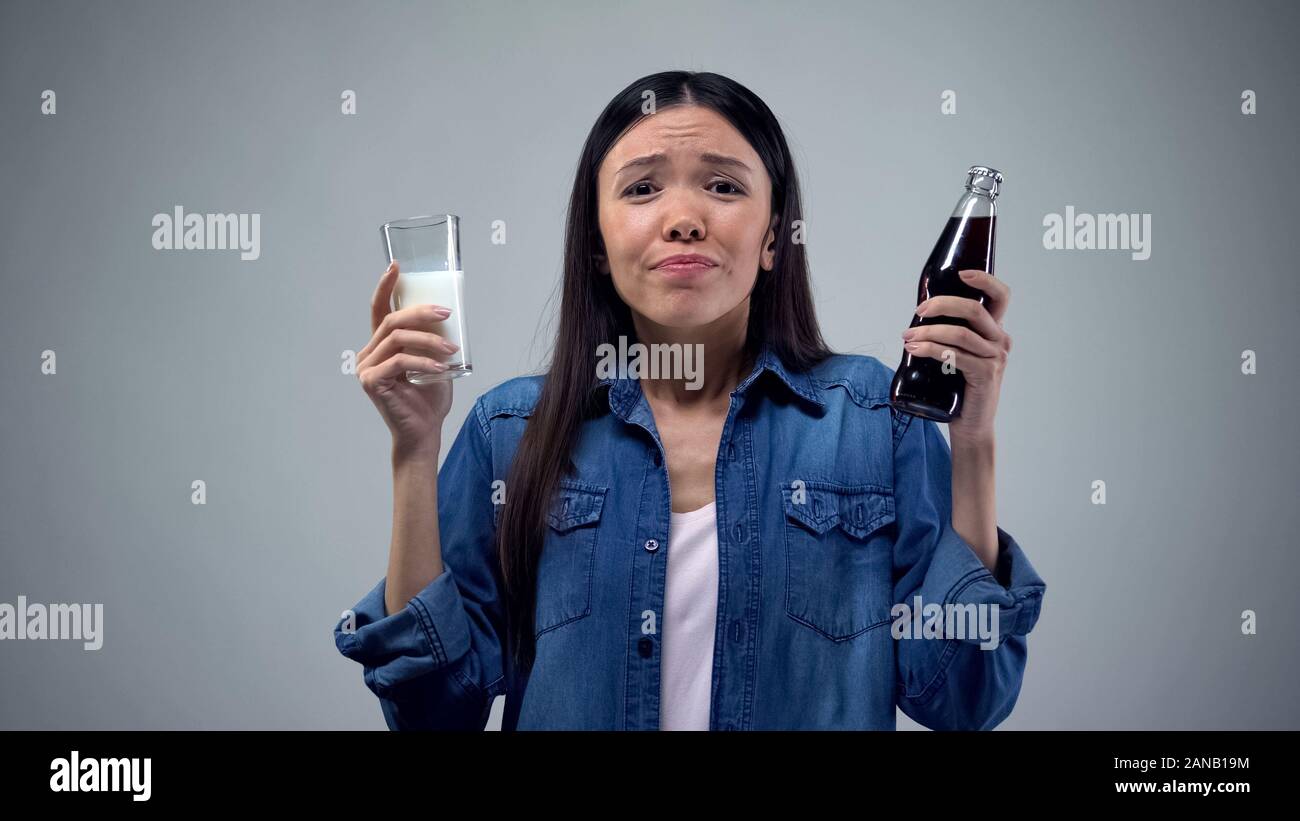 Woman trying to chose between unhealthy carbonated drink and useful healthy milk Stock Photo