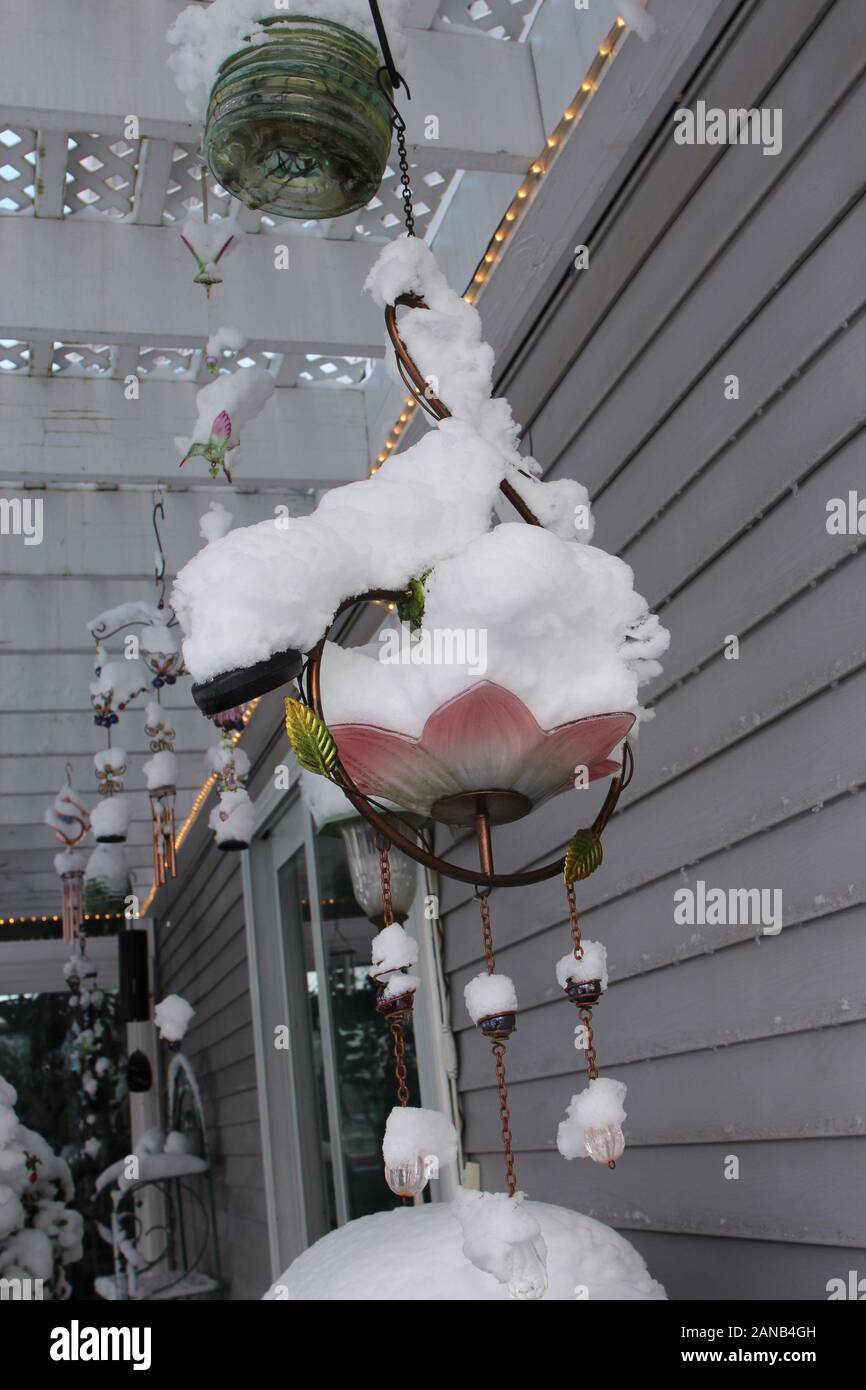 Outdoor windchimes and lanterns hanging from a pergola covered in snow