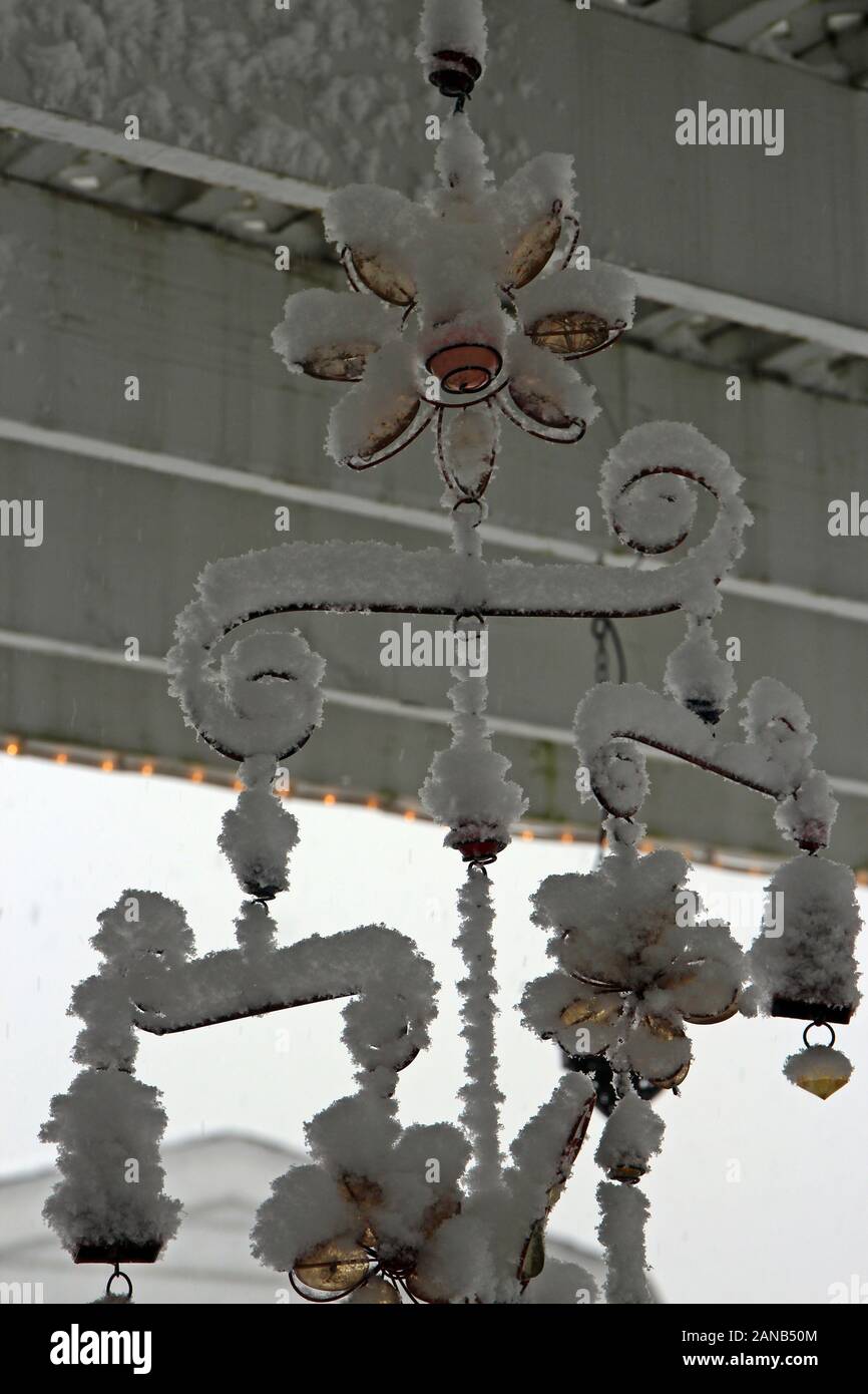 Close up of a glass flower windchime covered in snow hanging from a wood, white pergola in Wisconsin, USA Stock Photo
