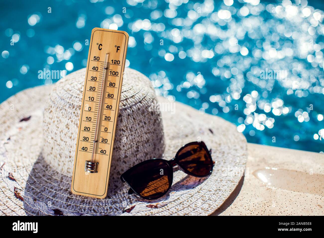 Woman's hat, thermometer and sunglasses lying beside the pool. Hot weather, summer and holiday concept Stock Photo