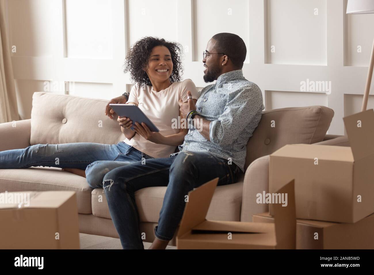 Smiling black family couple sitting on couch with tablet. Stock Photo