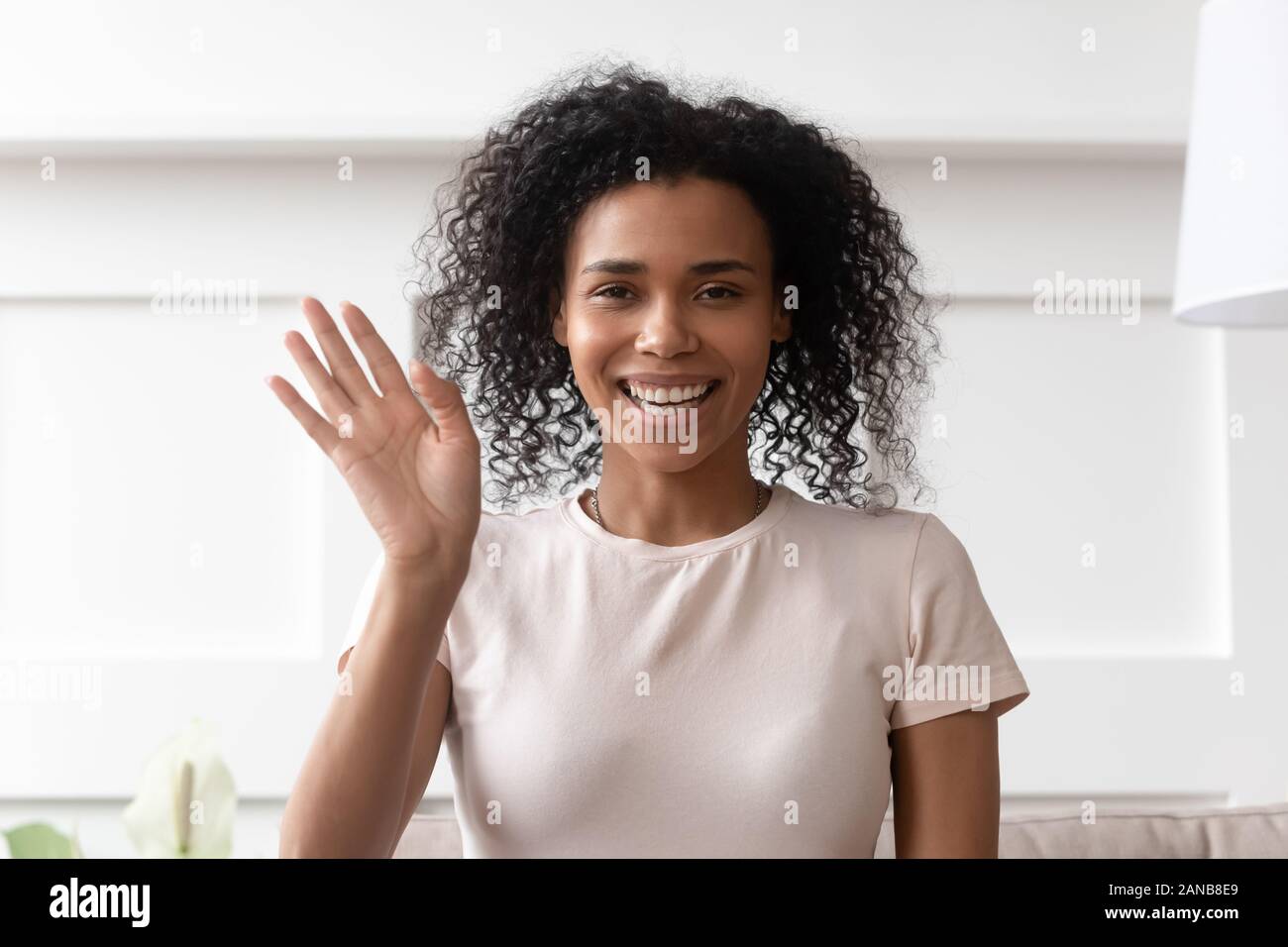 Smiling dark skinned curly lady waving hello. Stock Photo