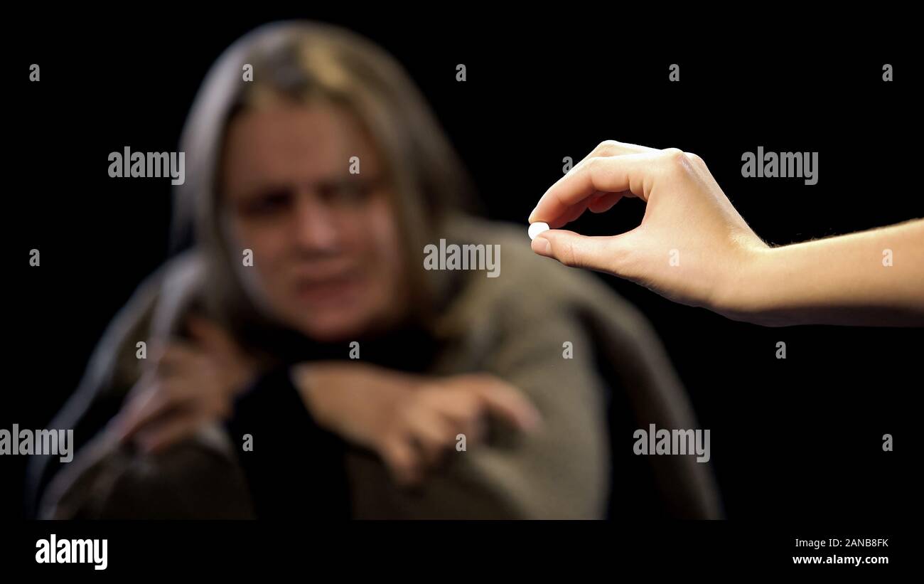 Hand offering LCD pill to woman suffering withdrawal symptoms, drug addiction Stock Photo