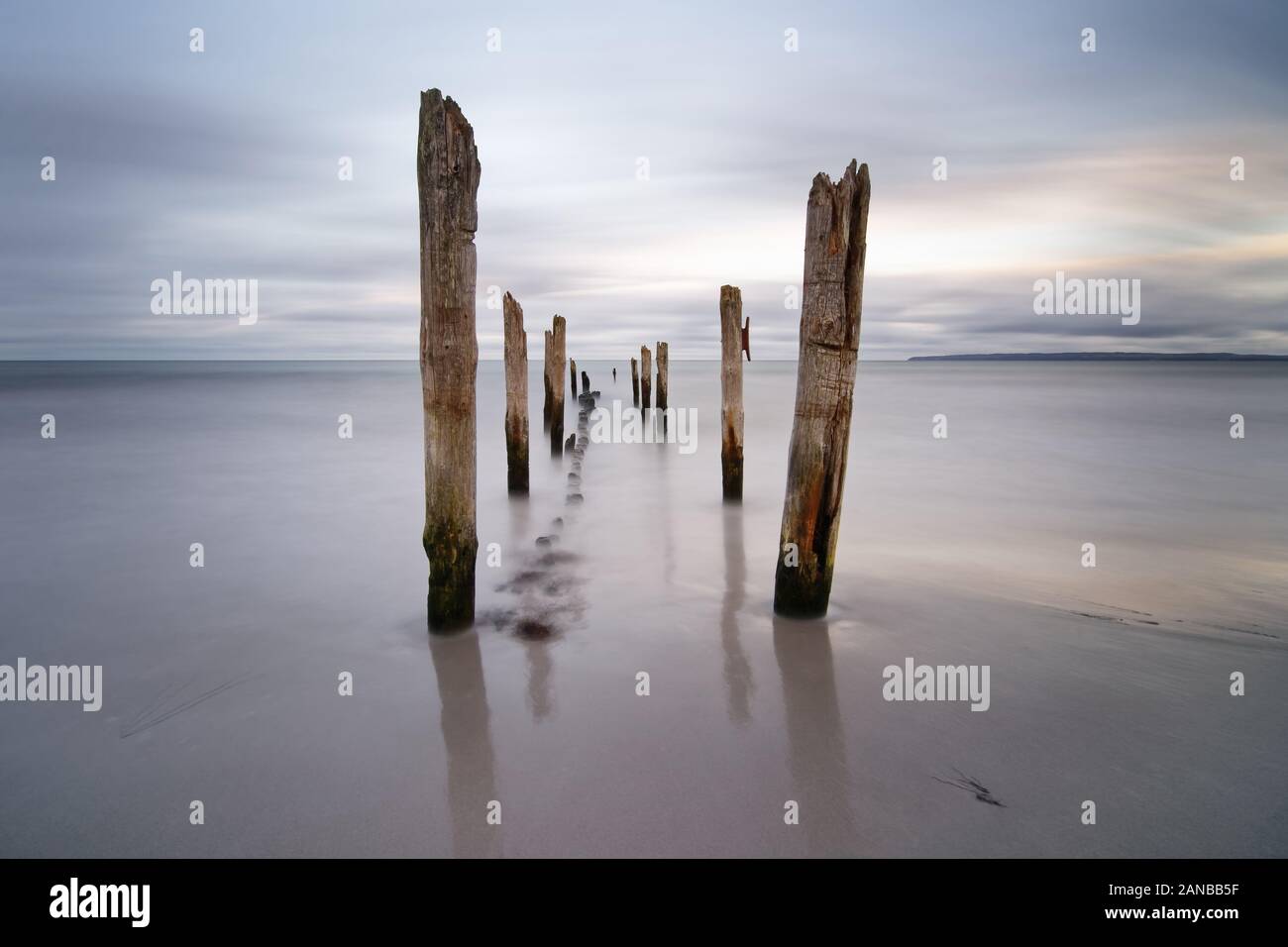 Wooden poles at the Baltic Sea beach in the evening light, water movement in long-term exposure, quiet melancholic mood, view guidance with depth effe Stock Photo