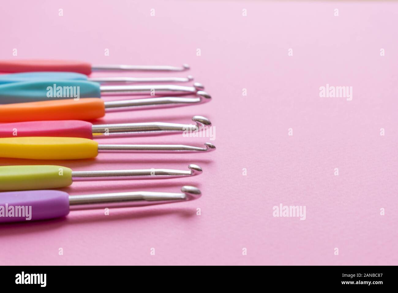 Closeup image of different size colorful crochet hooks on soft pink background Stock Photo