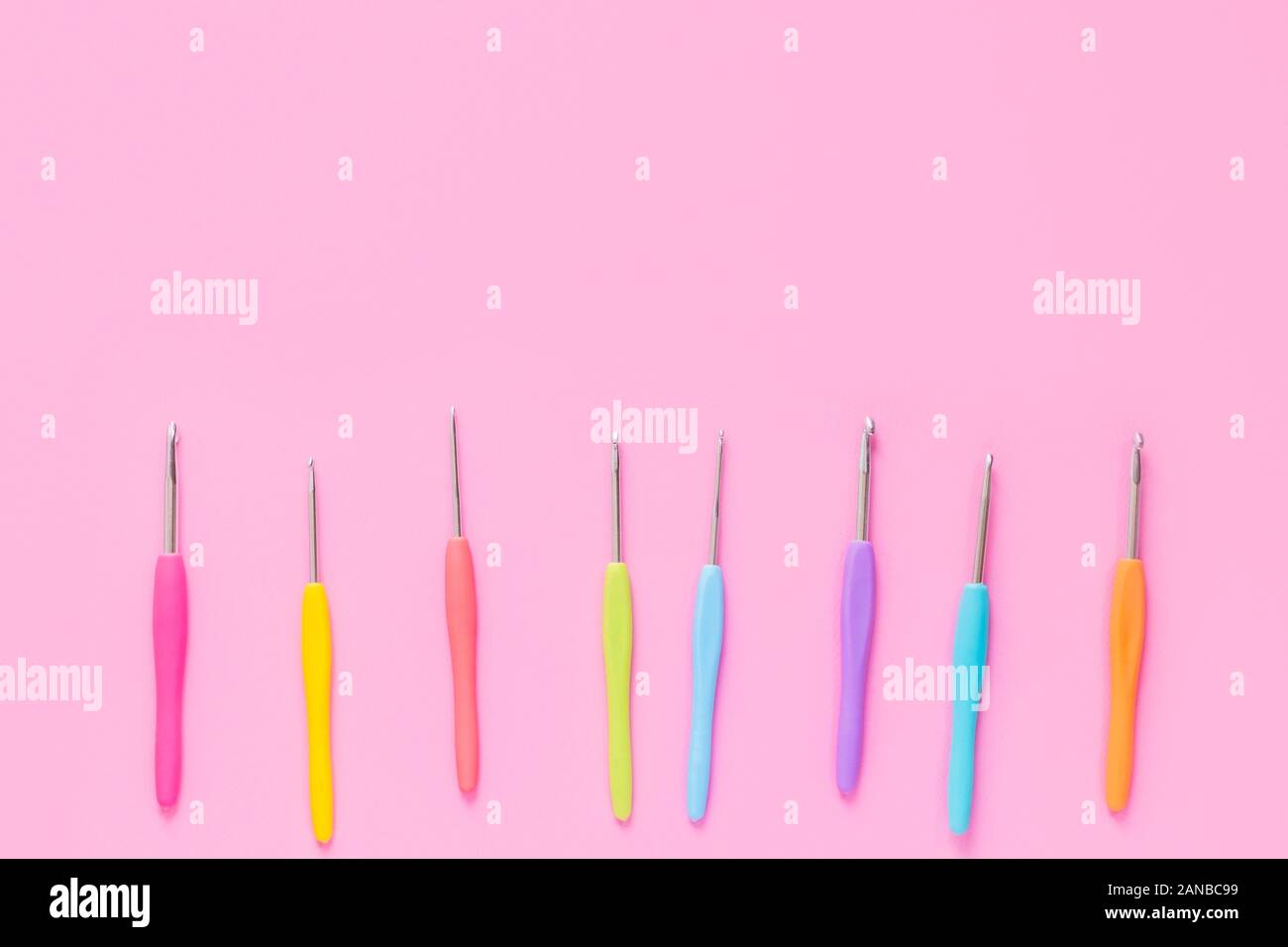 Various size bright crochet hooks on pink background Stock Photo