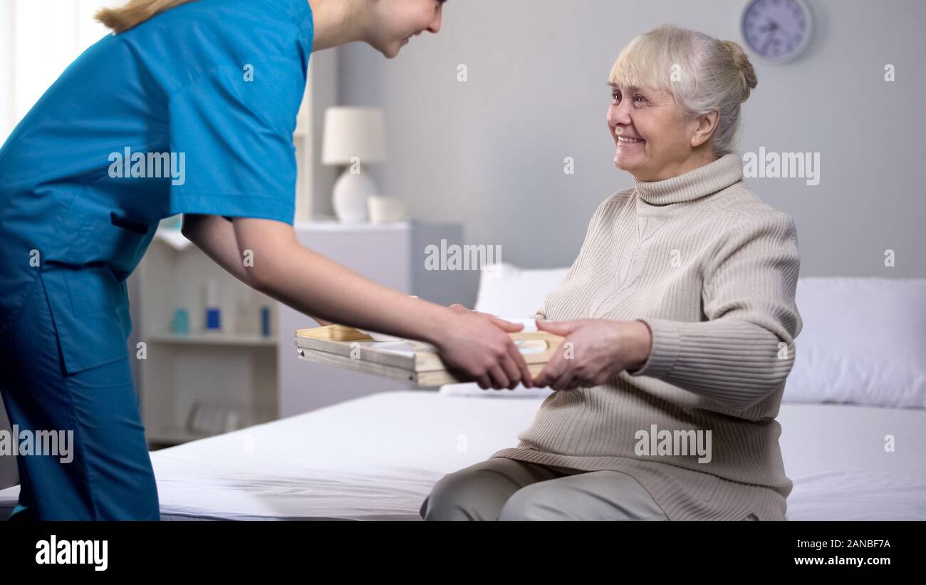 Medical worker serving dinner to old female patient, taking care of granny Stock Photo