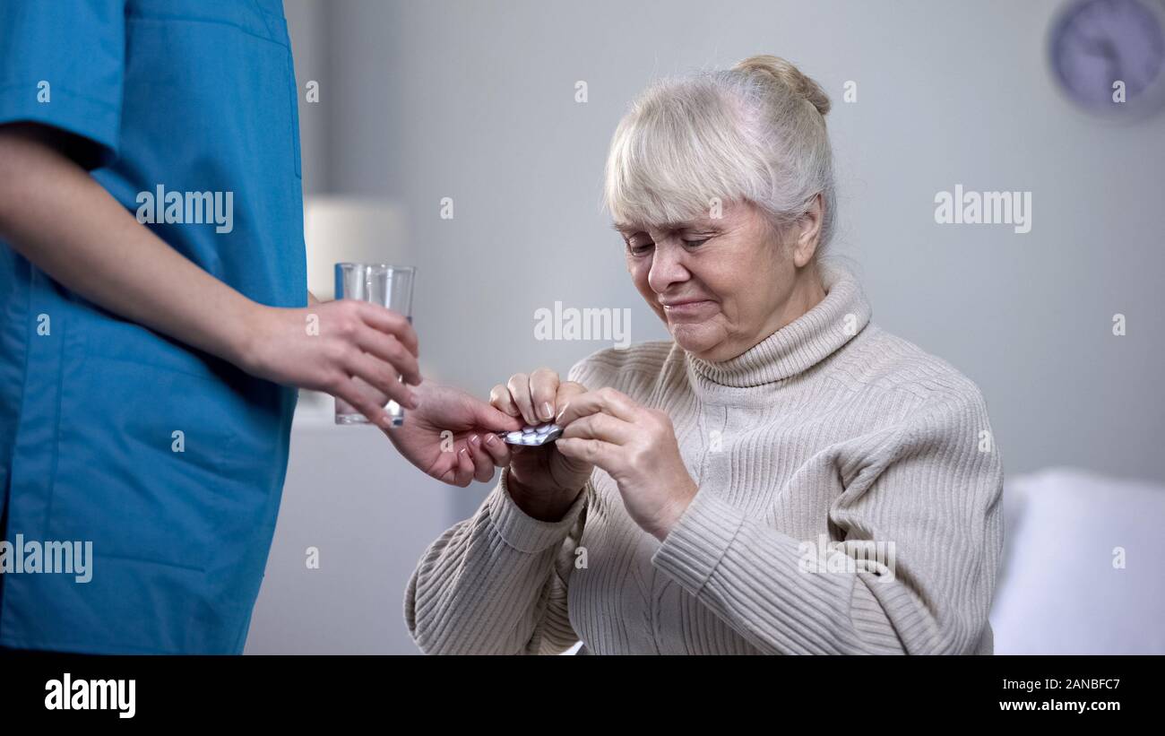 Nurse giving painkillers elderly woman suffering from headache, taking care Stock Photo