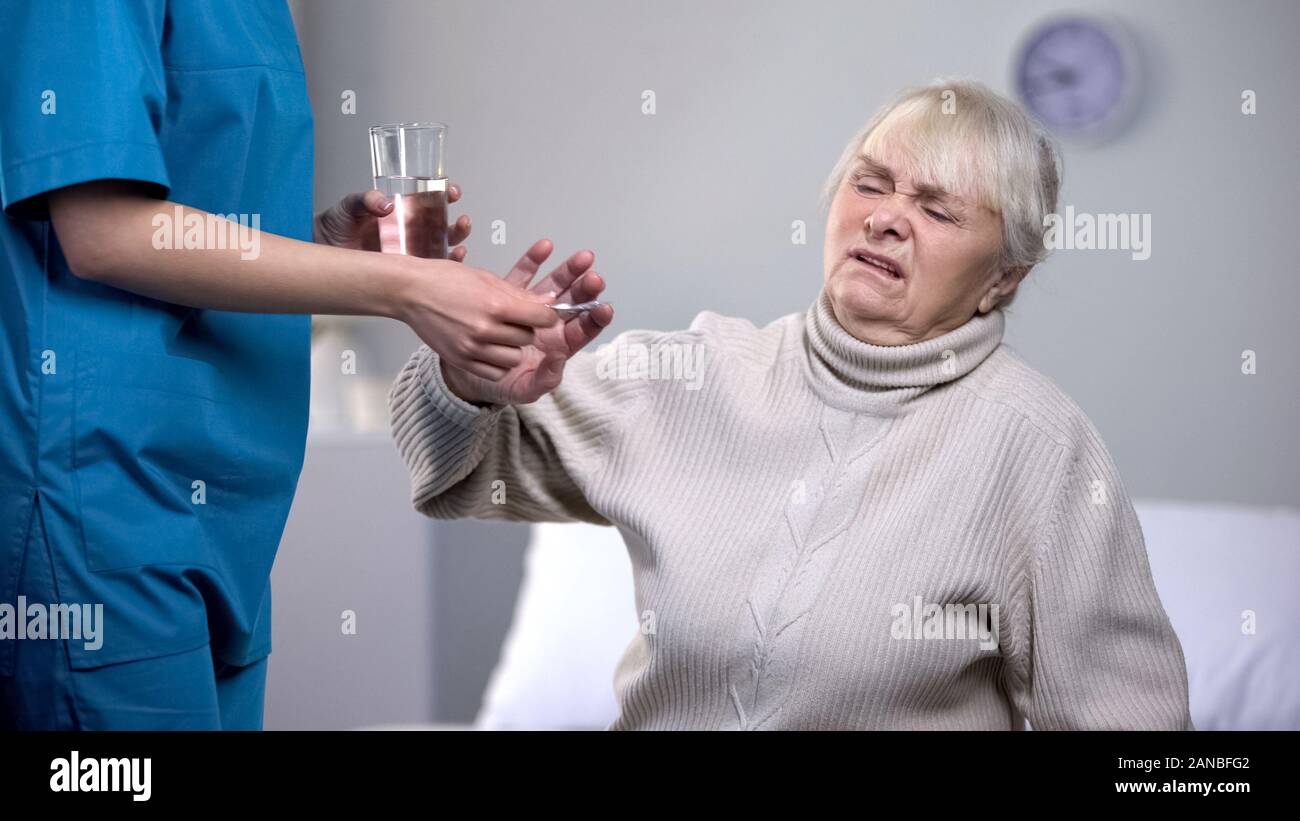 Capricious old woman rejecting medication from medical worker, treatment Stock Photo