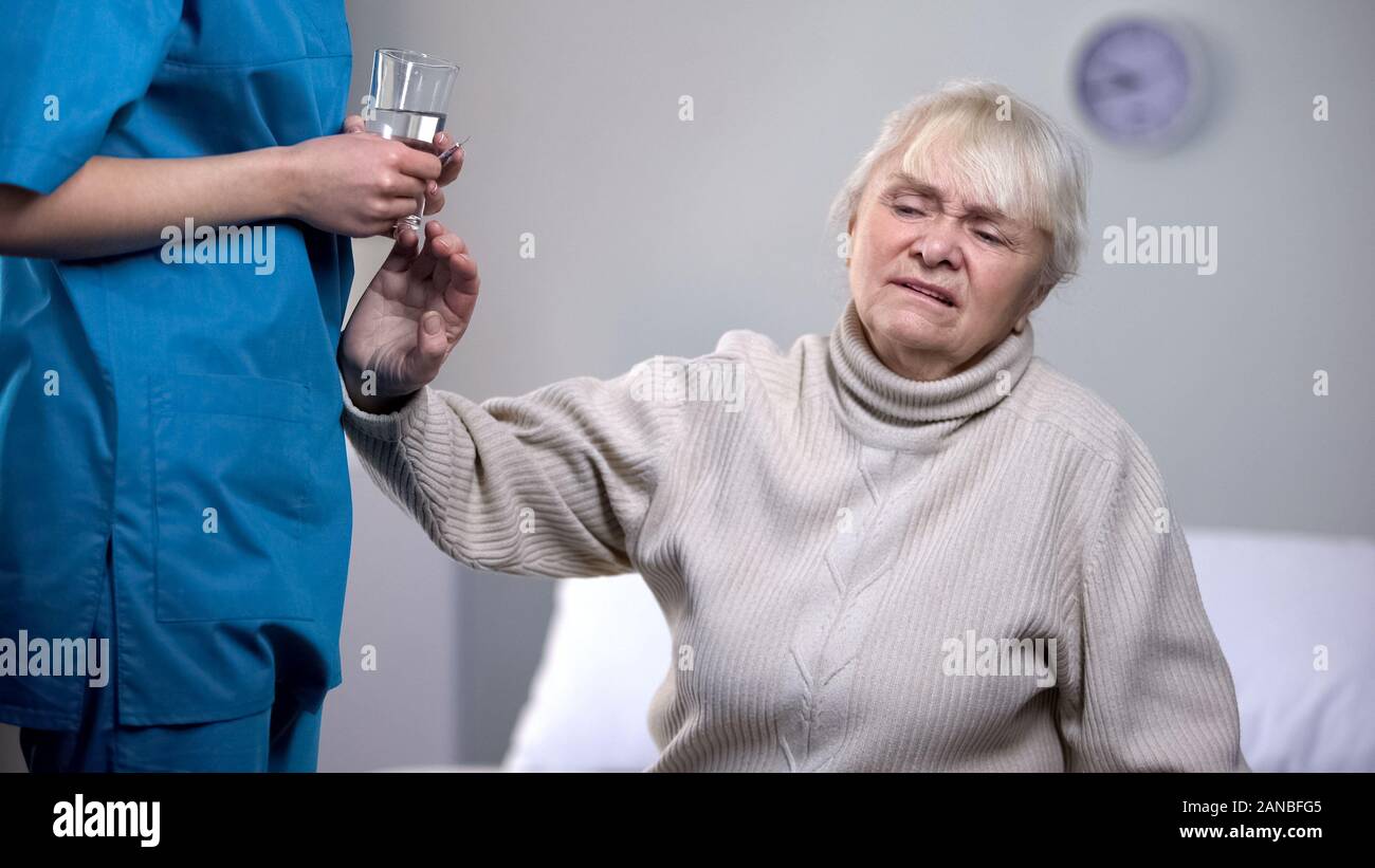 Old woman rejecting medication from nurse in rehabilitation center, treatment Stock Photo