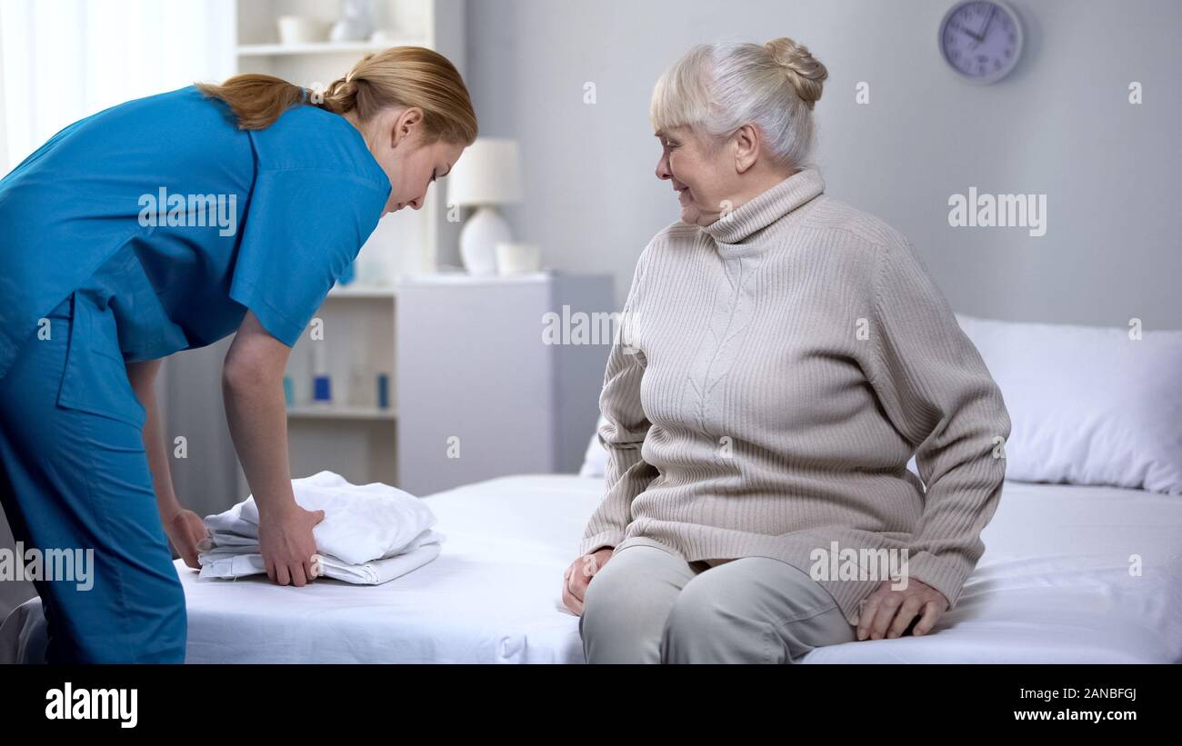 Nurse preparing clean bedlinen to elderly female patient in medical