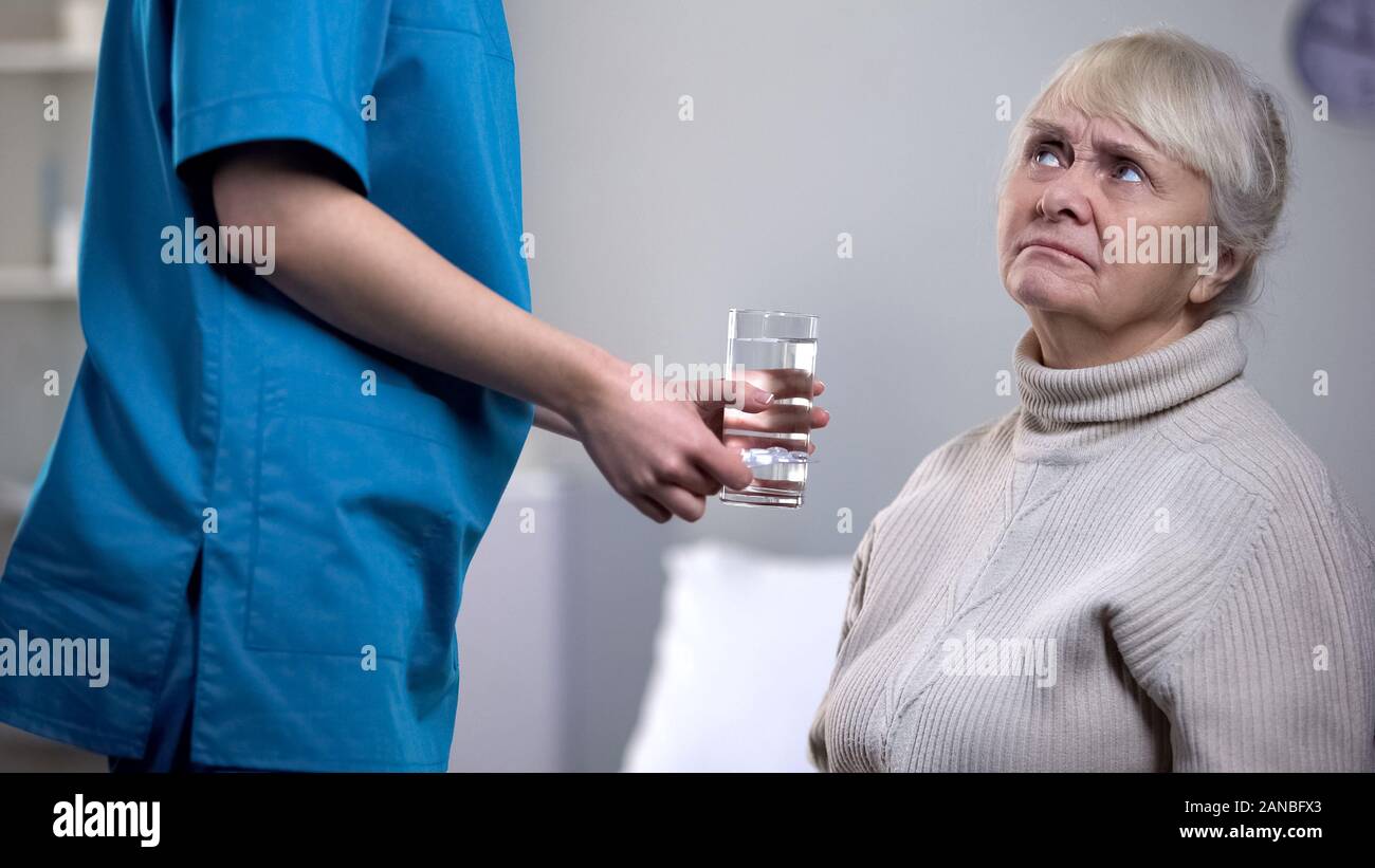 Dissatisfied elderly woman refusing pills from medical worker, nursing home Stock Photo