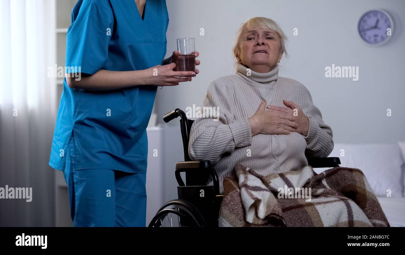 Female nurse giving pills and water glass old lay suffering chest pain, medicine Stock Photo