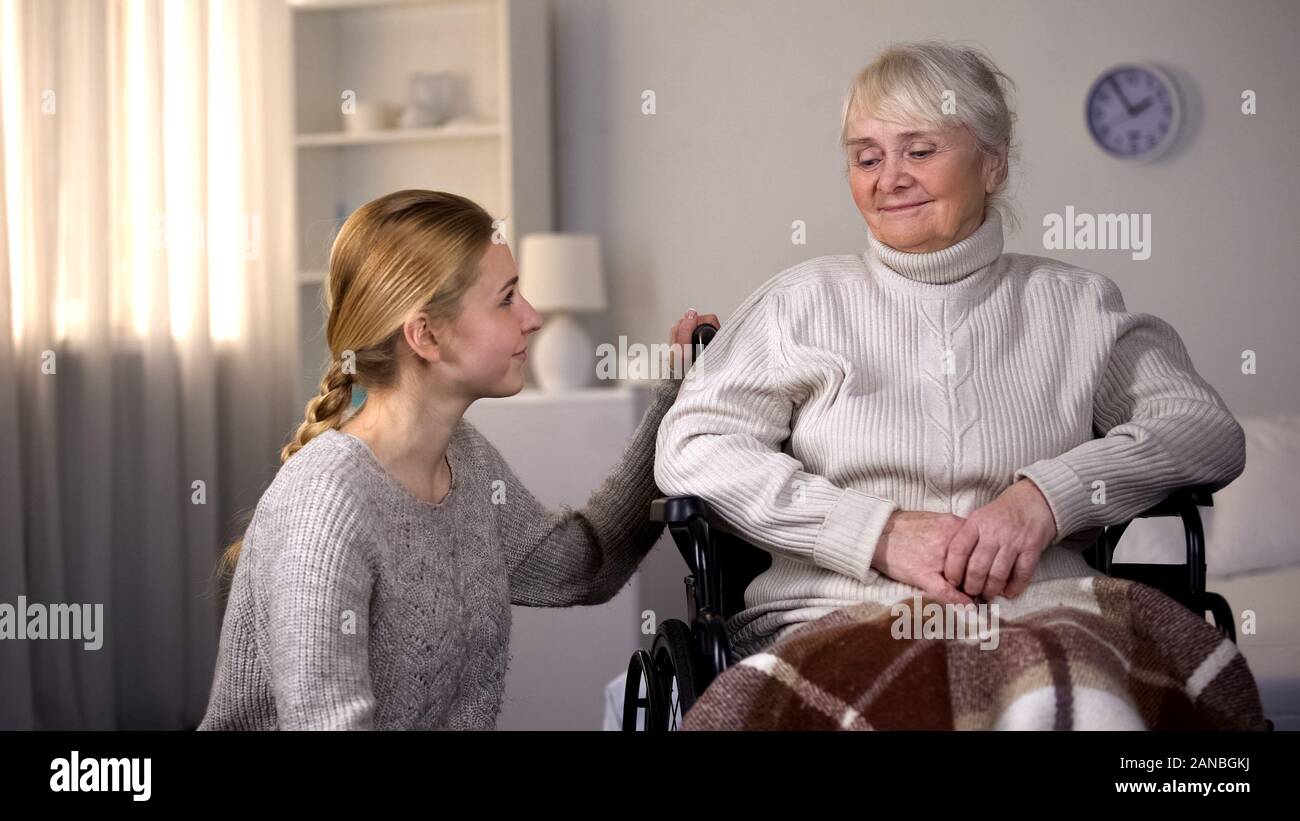 Granddaughter looking at handicapped granny, family care and support, hospital Stock Photo