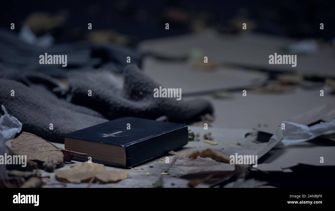 Bible lying on floor in dirty place full of garbage, hope and belief