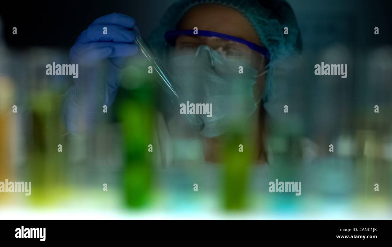 Lab assistant holding tube with blue test liquid, checking experiment ...