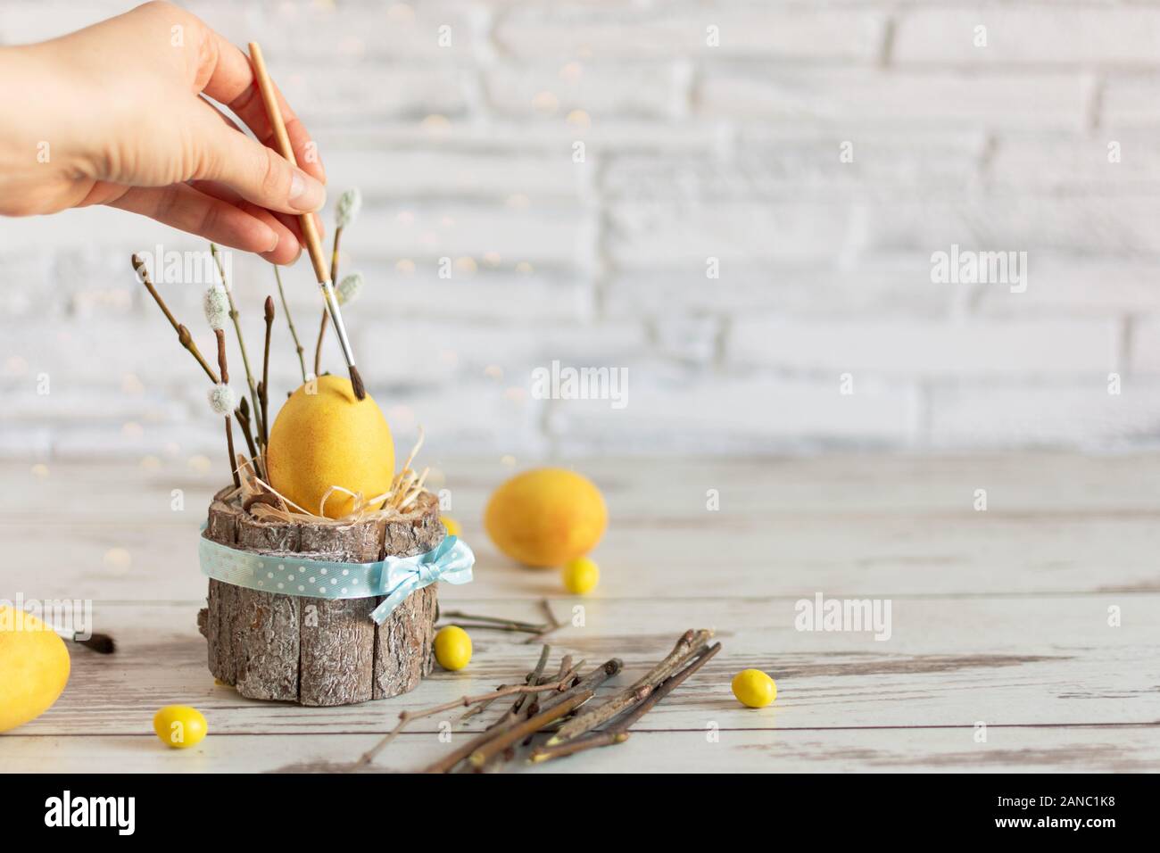 Woman hand paint Easter egg with paintbrush in modern matte yellow color on wooden table. Happy Easter time. Creative Easter decoration. Copy space. Stock Photo